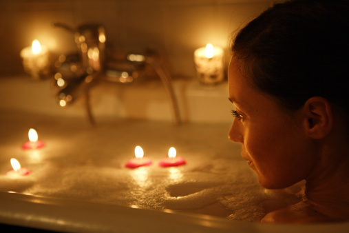 Žena odpočívající ve vaně zapálené svíčkami, boční pohled